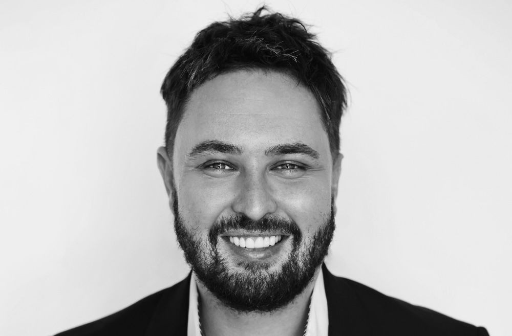 Smiling man with a beard in a black and white portrait.