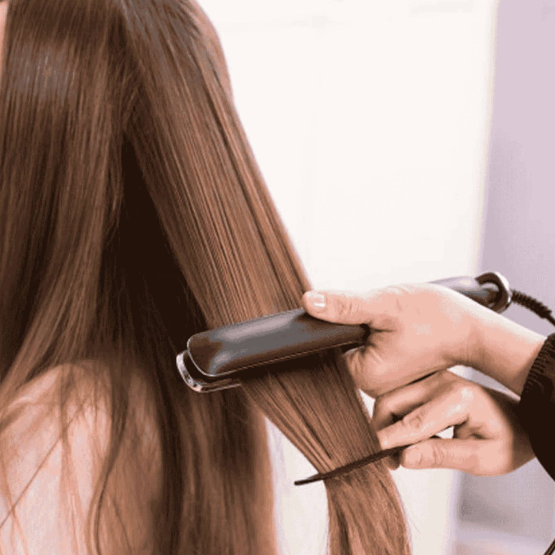 Person using a flat iron to straighten long brown hair.