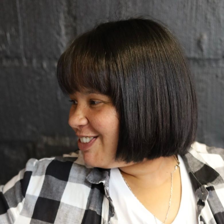 Person with a bob haircut in a checkered shirt, smiling and looking to the side.