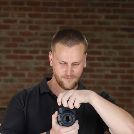 Person holding a camera in front of a brick wall.