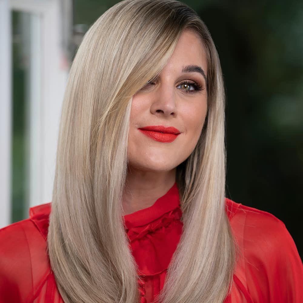 Woman with long blonde hair and red lipstick wearing a sheer red blouse.