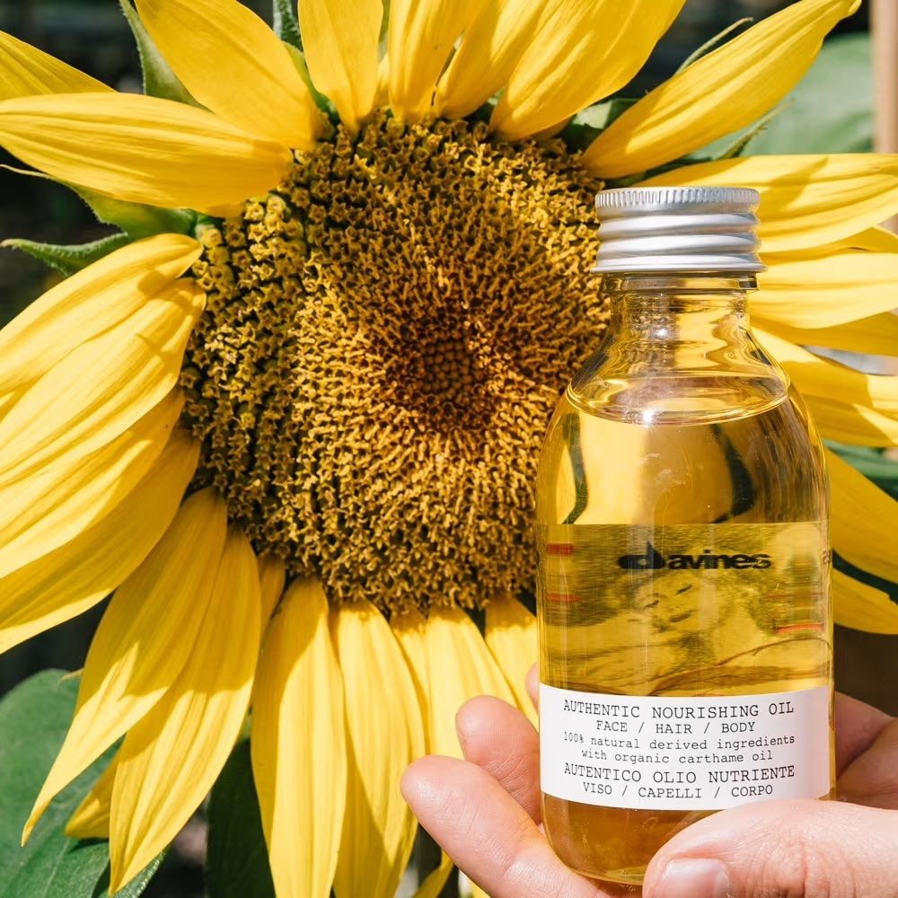 Hand holding a bottle of nourishing oil in front of a large sunflower in full bloom.